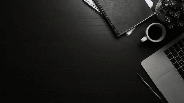 A quiet, focused workspace — notebook, coffee, and laptop on a dark desk